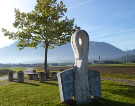 Zu sehen ist der Walser Birnbaum mit Denkmal, Sitzgruppe und Berg im Hintergrund