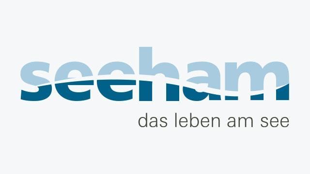 Das Logo der Gemeinde Seeham am Obertrumer See zeigt einen geschwungenen hell- und dunkelblauen Schriftzug des Ortsnamens, der an Wasser und Wellen erinnert - mit Untertext "das Leben am See".