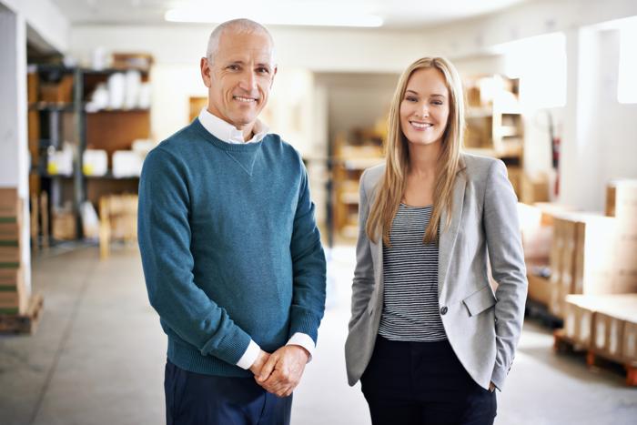 Zwei Unternehmerpersonen - wirken wie Vater und Tochter - sie aber fast selbstbewusster, stehen im Lager