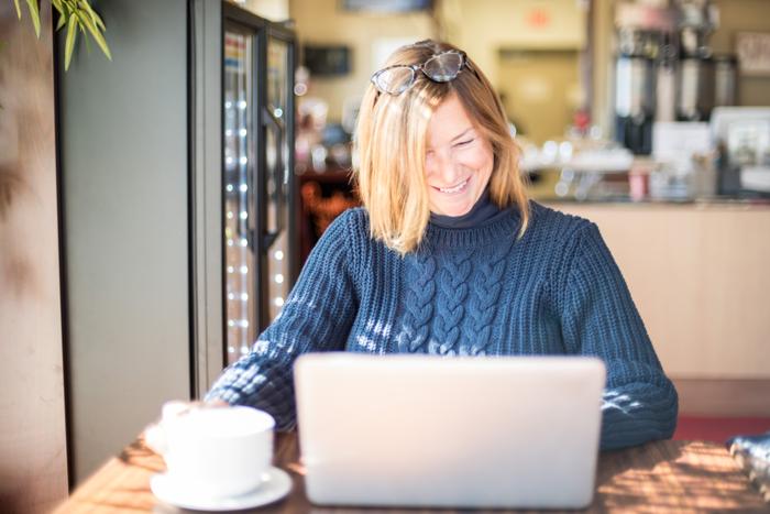 Ein Frau mittleren Alters schaut während ihrer Jobsuche in der Jobbörse Salzburg gut gelaunt in ihren Laptop 